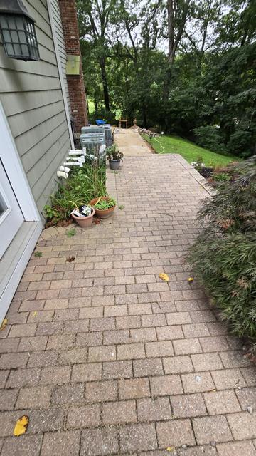 Long brick-style paver walkway running along the side of a house into a wooded backyard