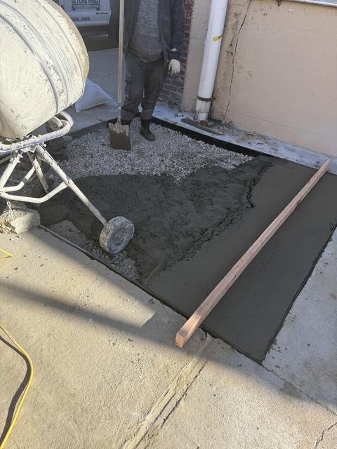 Concrete being placed from a mixer into a formed area next to a building