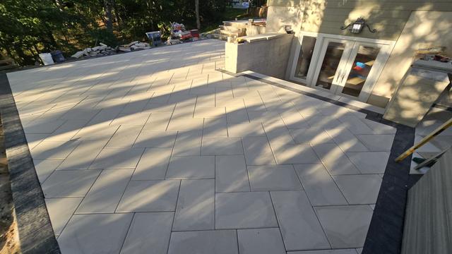 Wide backyard patio of large-format light gray porcelain pavers with a dark border