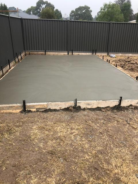 New concrete slab poured in a backyard in front of a black privacy fence