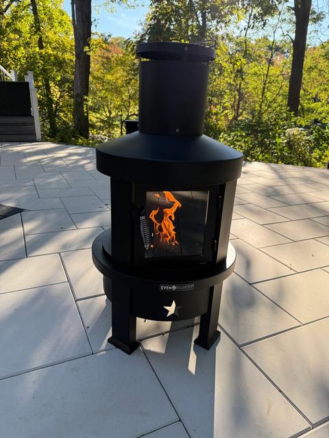 Black steel wood-burning fire feature lit on a light gray large-format porcelain patio